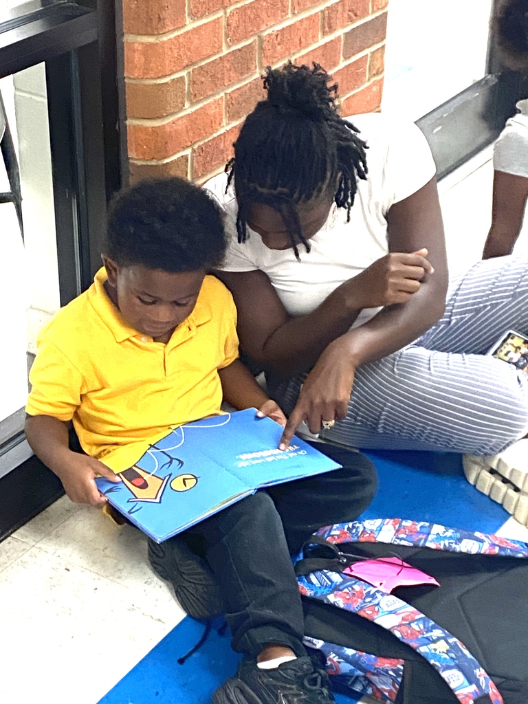 teacher and student sitting on hallway floor, reading the same book together