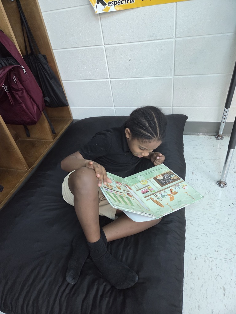 male student sitting on floor cushion while reading a book
