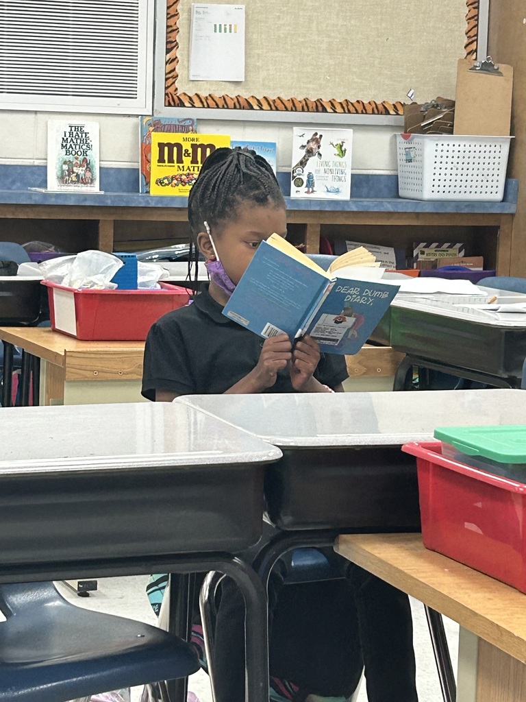 student reading a blue book while sitting at their desk. Book is covering most of their face