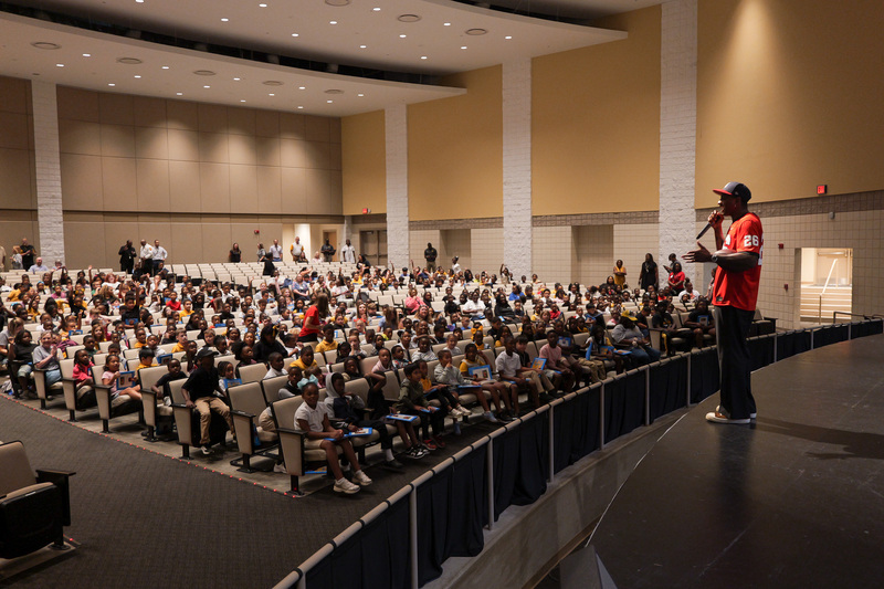 Wide shot of students in performing arts center while Malcolm is speaking on the stage