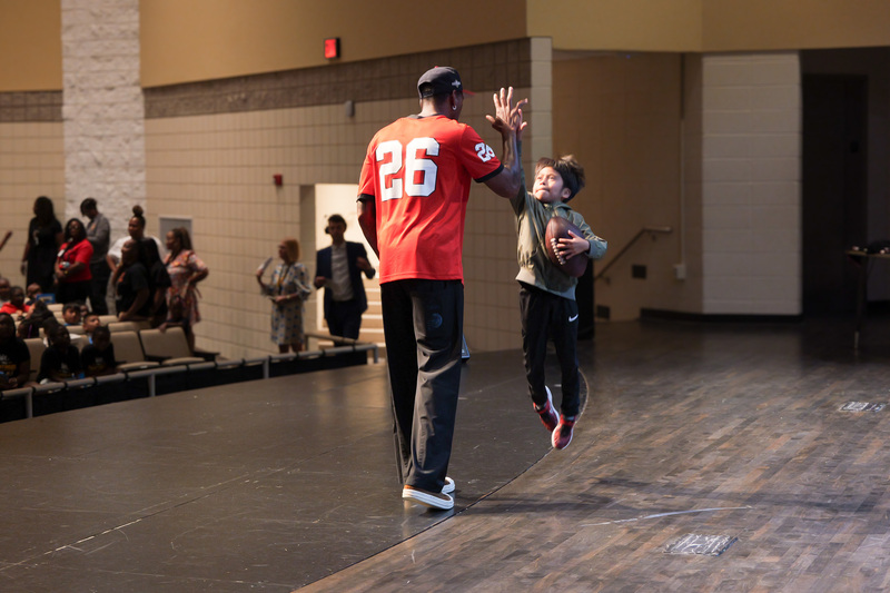 kid high fiving Malcolm, jumping in the air to reach while holding a football