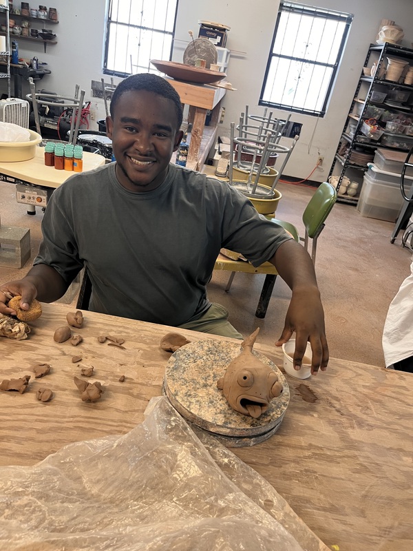 art teacher smiling with his pottery of a fish character on a plate in front of him