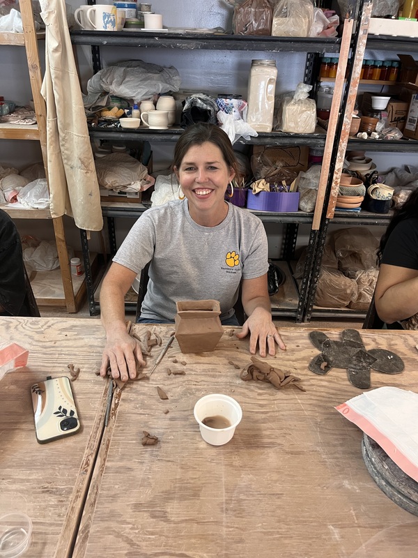 Art teacher smiling with hands on each side of her pottery that appears to be a vase