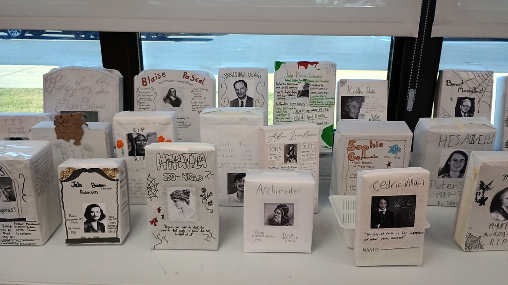 🪦 A "Grave" Exploration of Math History: Our 8th Grade Mathematician Graveyard This fall, our 8th graders brought history — and math — to life (or perhaps afterlife) through a creative research project on famous mathematicians. Each student chose a notable figure from the world of mathematics, from Pythagoras to Katherine Johnson, and dug deep into their lives, discoveries, and lasting impact. But instead of presenting their findings in a typical report or slideshow, students designed tombstones to represent their chosen mathematician. Each tombstone included key details like birth and death dates, major contributions to the field, fun facts, and even clever epitaphs that captured the mathematician’s legacy. The result? A one-of-a-kind Mathematician Graveyard that transformed Mrs. Schlotzhauer's classroom into an interactive exhibit of mathematical history. As students walked through the graveyard, they explored centuries of mathematical thought — from geometry and algebra to probability and logic — all while appreciating how each thinker’s ideas continue to shape the math we use today. The project combined research, creativity, and visual storytelling, giving students a chance to connect with the human side of mathematics. It also sparked some great conversations: Who really discovered zero? What challenges did women in math face in earlier centuries? And how have modern mathematicians built on the ideas of those who came before? Whether spooky, serious, or just plain smart, each tombstone reflected not just the mathematician’s story, but the student’s own curiosity and voice. We’re so proud of our young historians and mathematicians for making this project both educational and unforgettable. Ask your 8th graders about the “graveyard” this week — if you dare — and see for yourself how our 8th graders are keeping math alive in the most creative way possible!