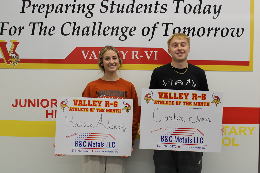 Two students posing in front of wall for athlete of the month photo