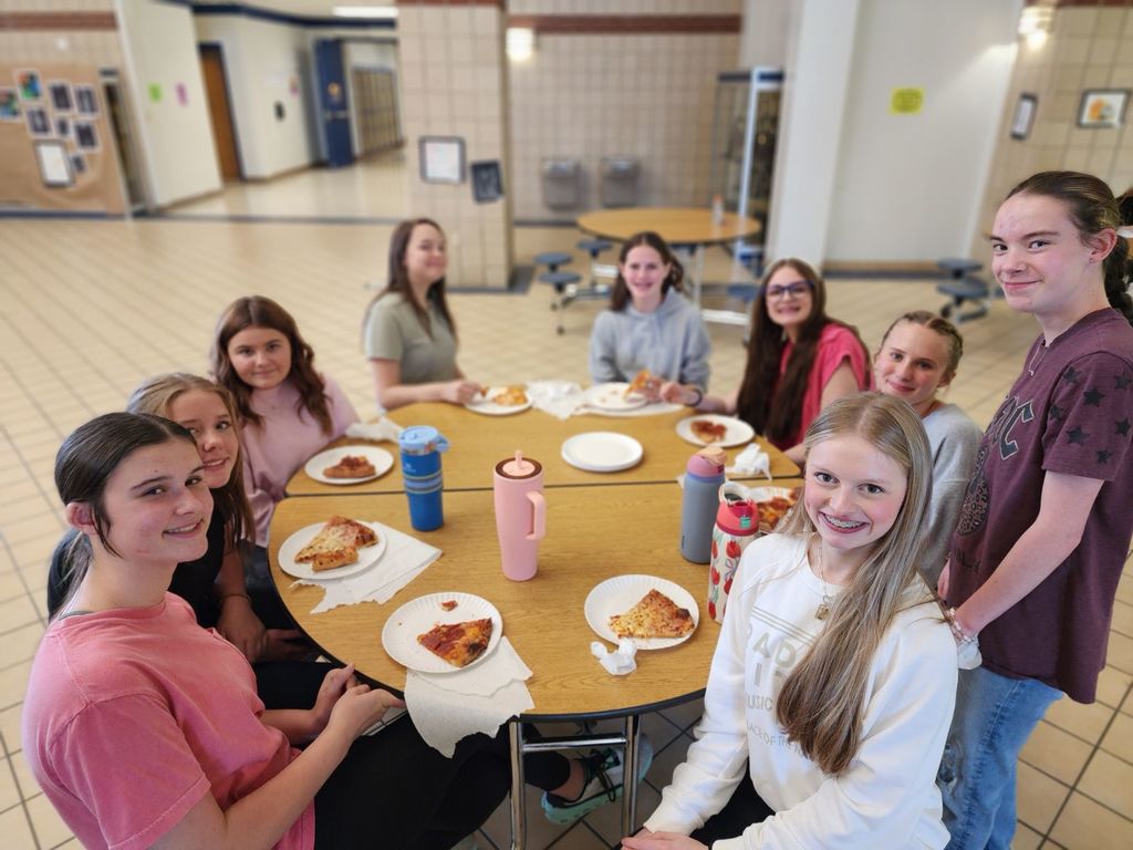 girls seated at a table eating pizza