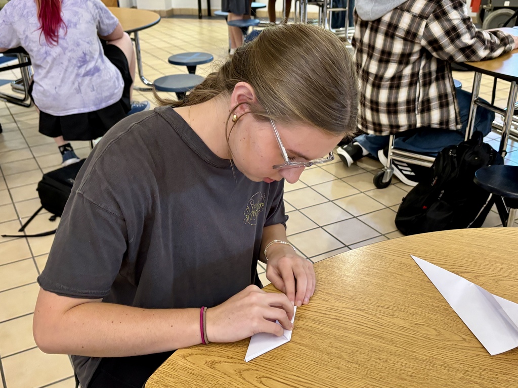a girl folding a paper airplane at a table