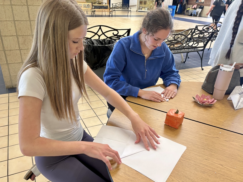 two girls folding planes at a table