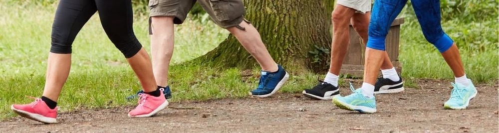 image of 4 adults walking in tennis shoes. They are all walking on dirt near a grassy area and it just shows their calves and feet.