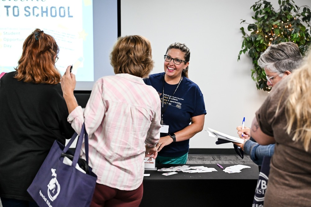 Photo of Monica Mansfield smiling and handing out flyers and paperwork to a couple of ladies. They have their backs to the camera.