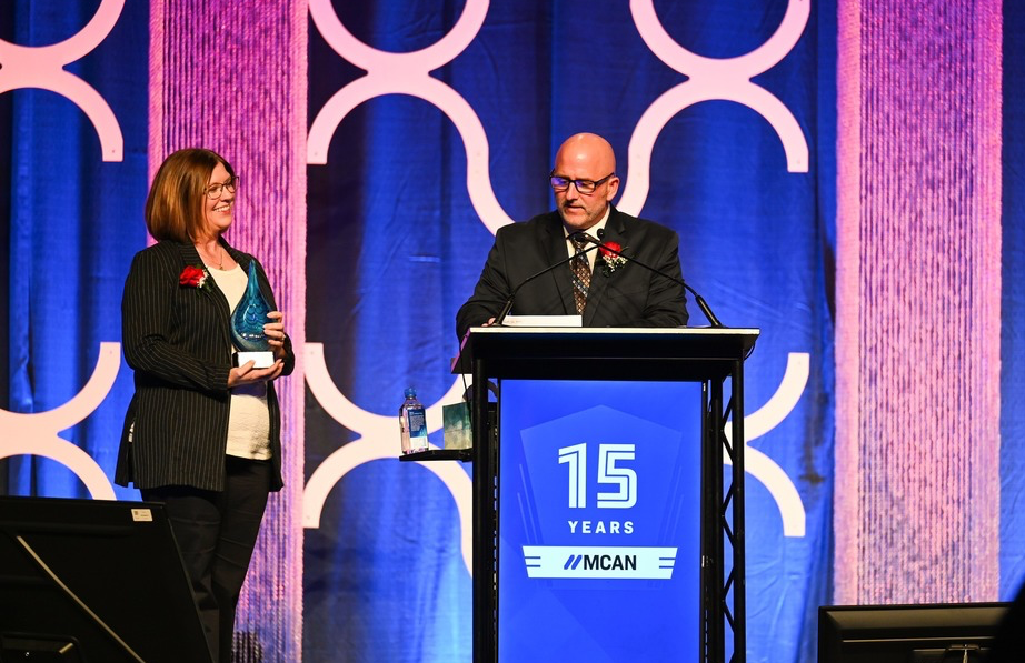 photo of robert smith speaking in a microphone at a podium with a woman next to him standing and smiling holding a trophy.