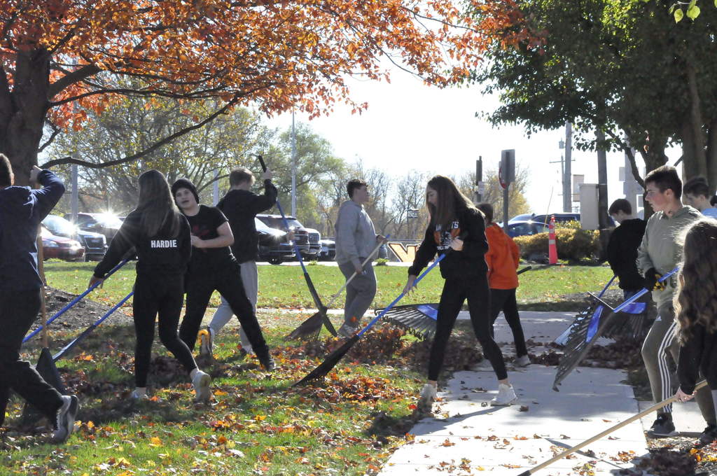 Students rake leaves in front of the school.