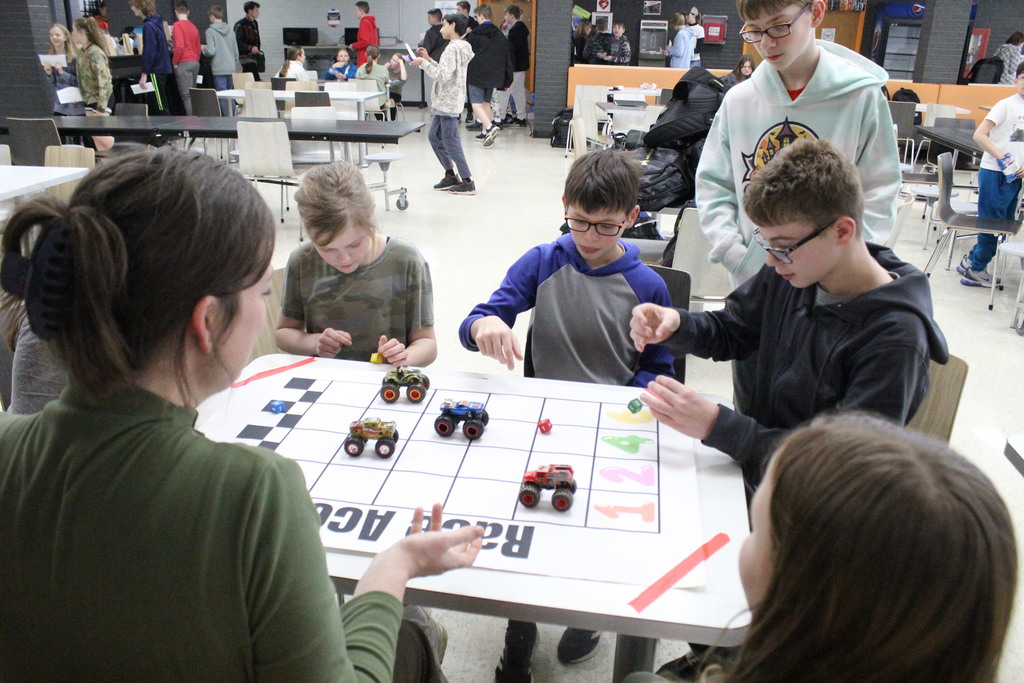 Students play a game where they are each required to roll a die, and based on the result, they move their cars. Whoever reaches the finish line first wins!