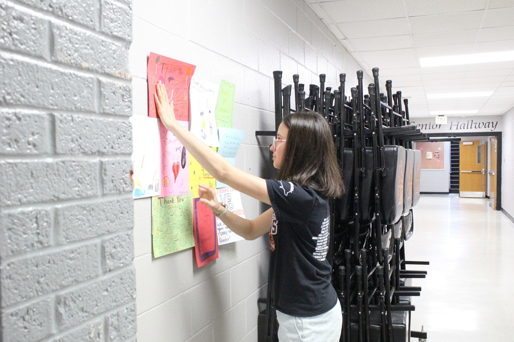 Sadie hangs one of her collages in the high school.