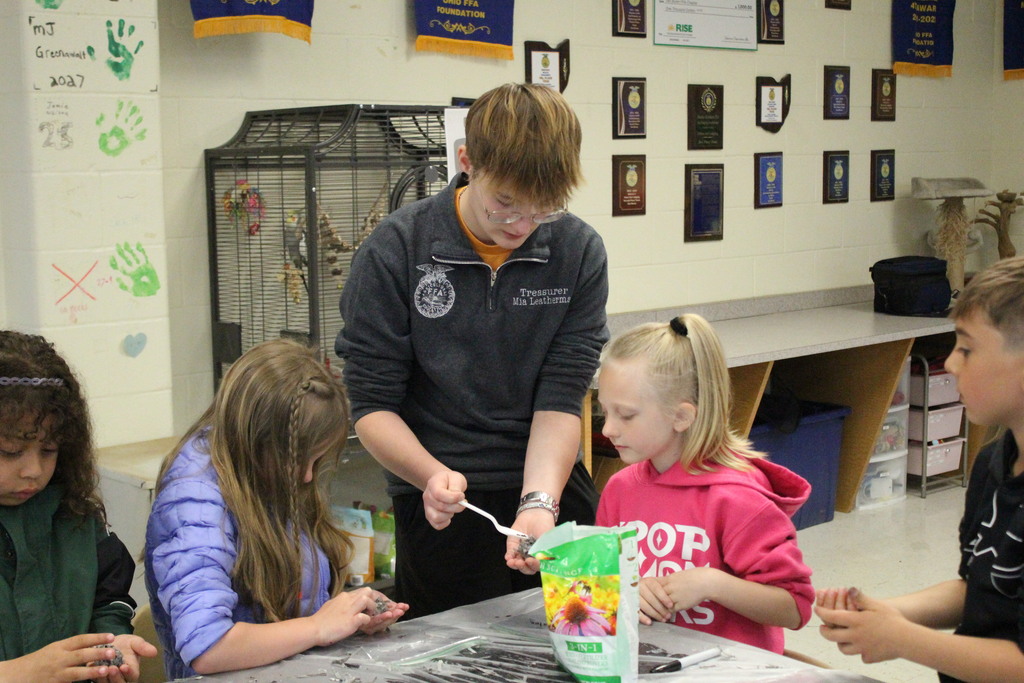 An agriculture education student adds the seeds to the pod while elementary students observe.