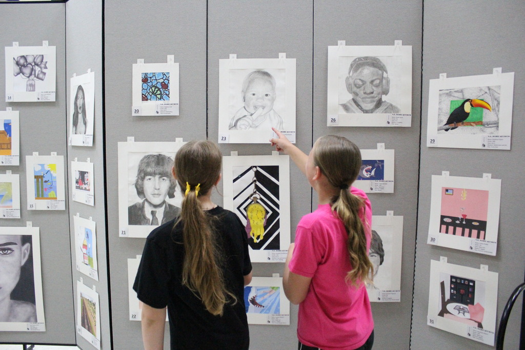 Students observe the artwork at the art show.