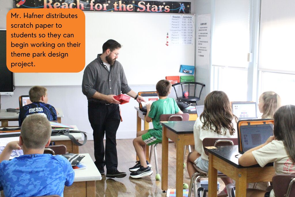 A picture showing Mr. Hafner as he distributes scratch paper to students so they can begin working on their theme park design project.