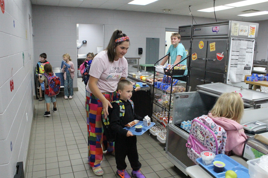 A picture of Mrs. May helping an elementary student pick up his breakfast on Monday, September 14, the first day breakfast was served.