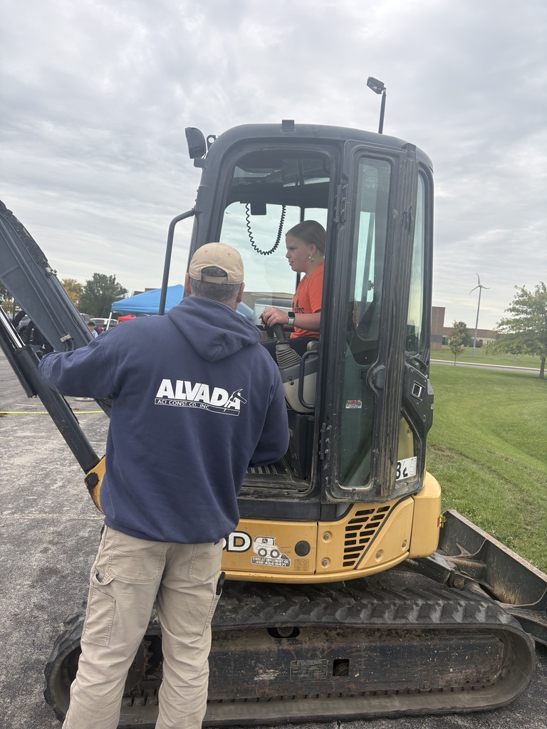 A picture of a student maneuvering a backhoe under the guidance of a representative of Alvada Construction.
