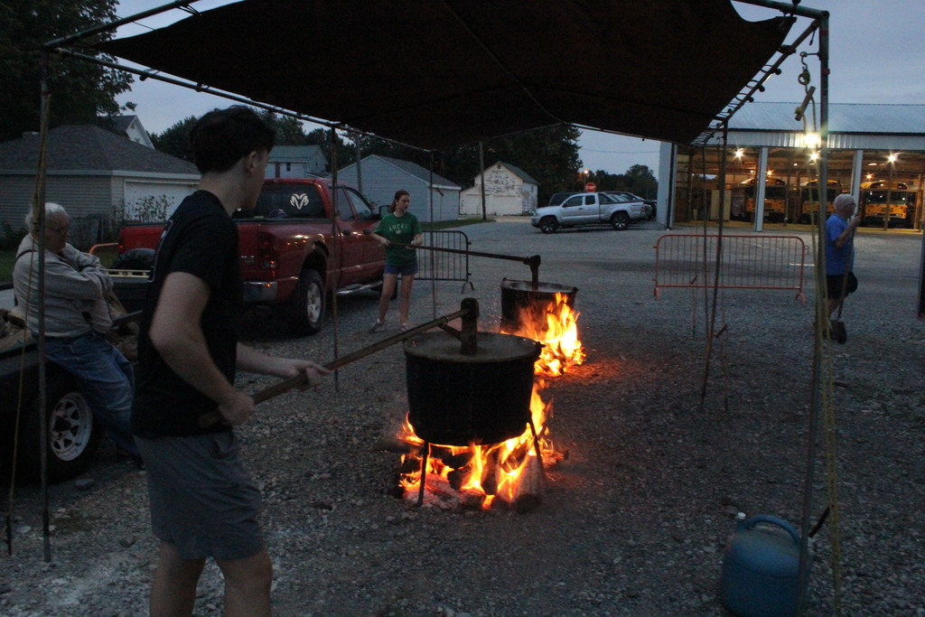 A picture of FFA students stirring what will become apple butter as it cooks in a copper kettle over an open flame.
