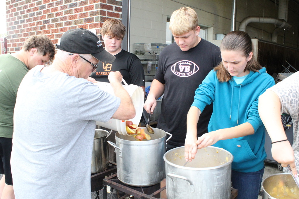 A picture showing Van Buren Mayor Ed May pouring sliced apples into a pot to be cooked while students stir the cooking apples.