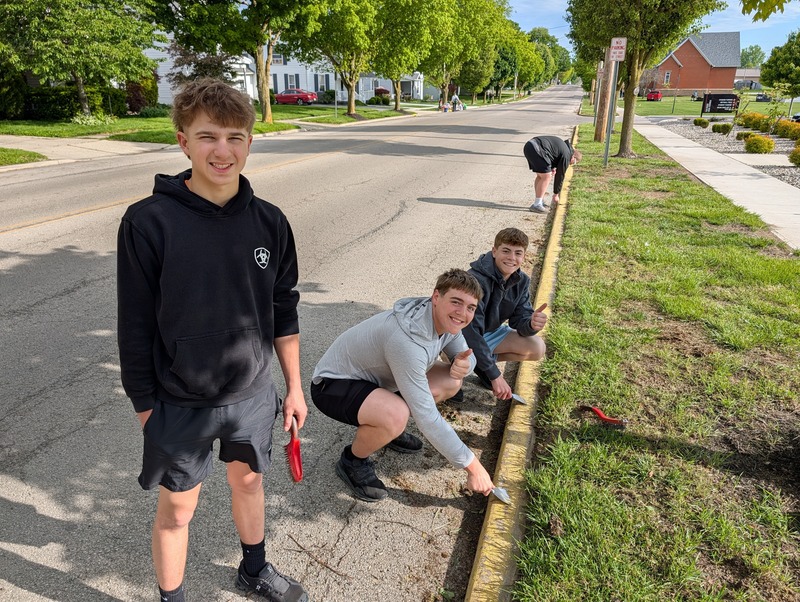 Students scrape the curbs in front of the school to prepare them to be painted.