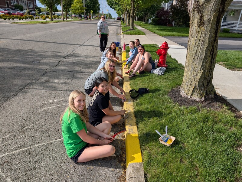 Students scrape and paint curbs in the village.
