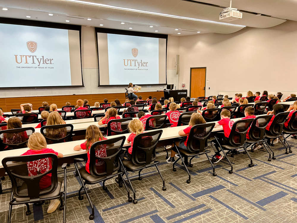 students face the front of the room in a lecture hall with a teacher in front