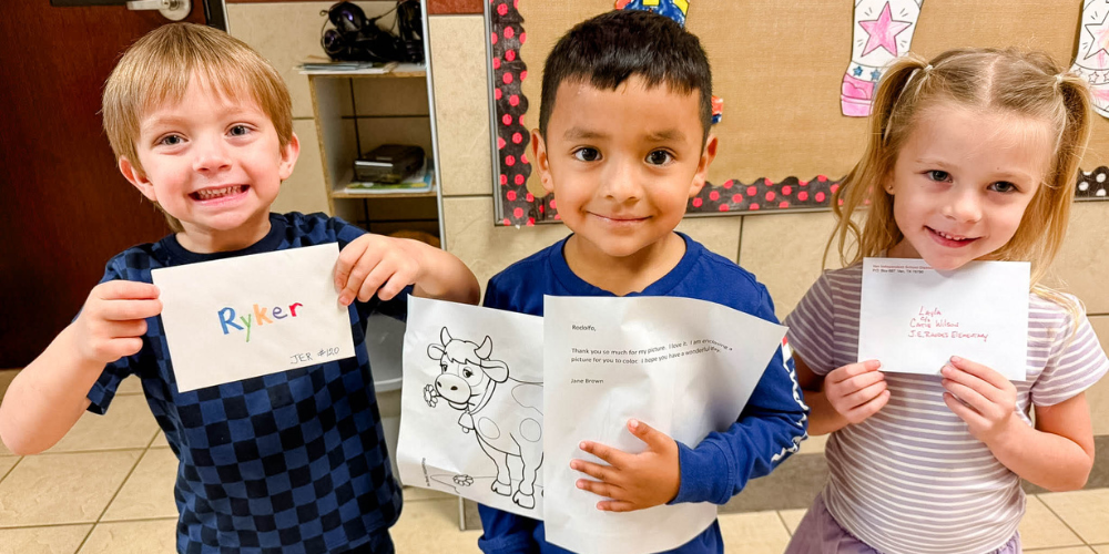 3 students holding up letters and smiling