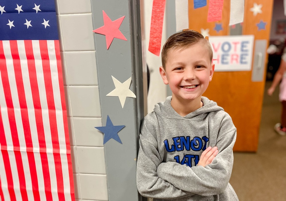 student smiling next to american flag