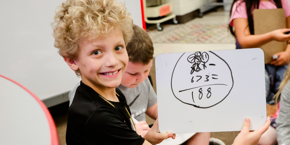 student holding up a whiteboard with a math problem written on it