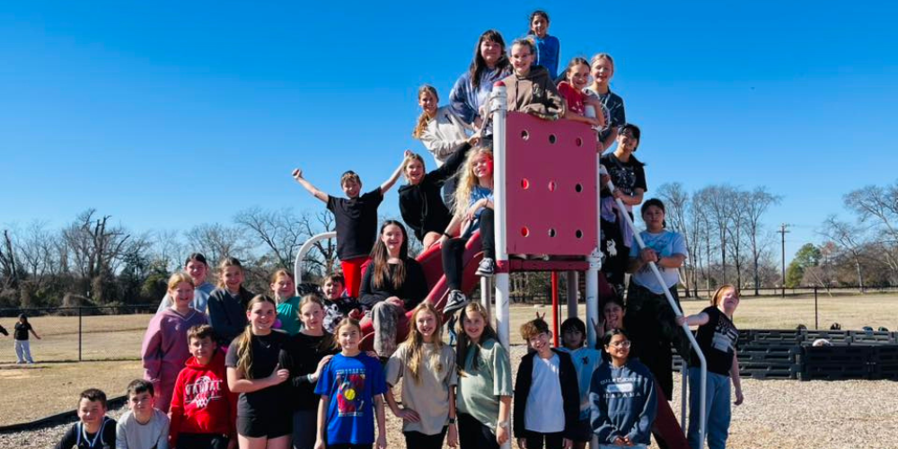 6th graders stand on playground equipment
