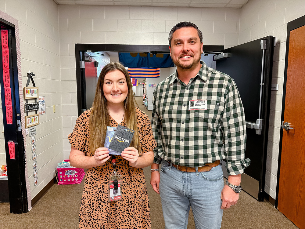 Emily Brown & Zach Pruitt stand together in a hallway holding gift cards
