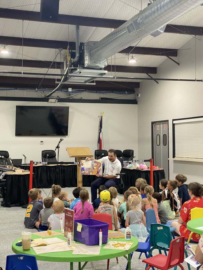 Man reading a book to children in a library.