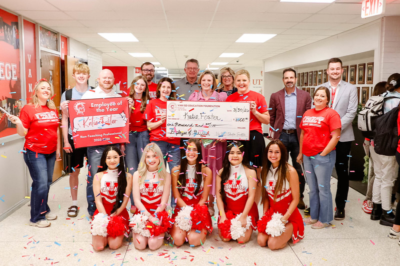 teacher of the year holding a check for $1,000 and cheerleaders and confetti surrounding them