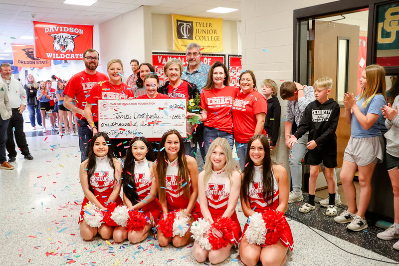teacher of the year holding a check for $1,000 and cheerleaders and confetti surrounding them