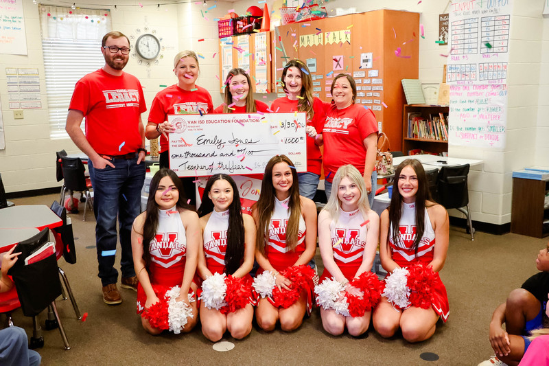 teacher of the year holding a check for $1,000 and cheerleaders and confetti surrounding them