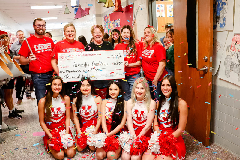 teacher of the year holding a check for $1,000 and cheerleaders and confetti surrounding them
