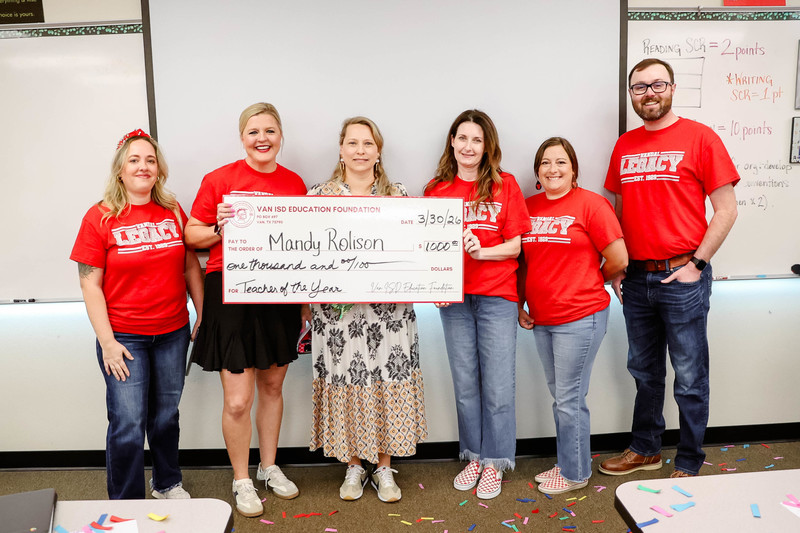teacher of the year holding a check for $1,000 and cheerleaders and confetti surrounding them