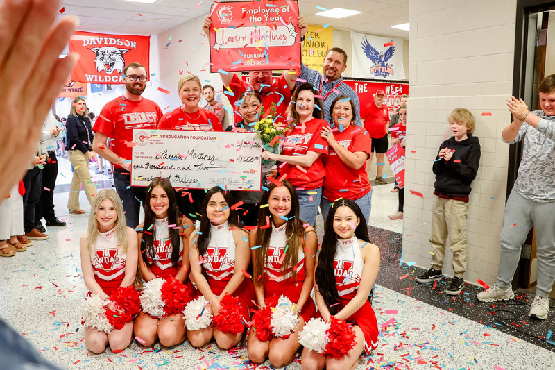 teacher of the year holding a check for $1,000 and cheerleaders and confetti surrounding them
