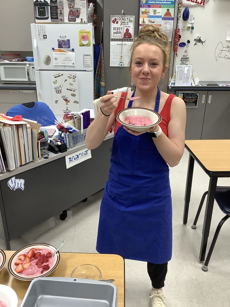 Student smiling and eating a strawberry smoothie in a bowl.