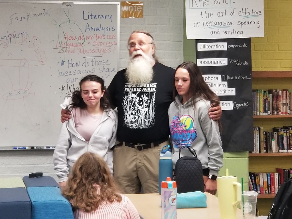 Classroom speaker hugging two girl students