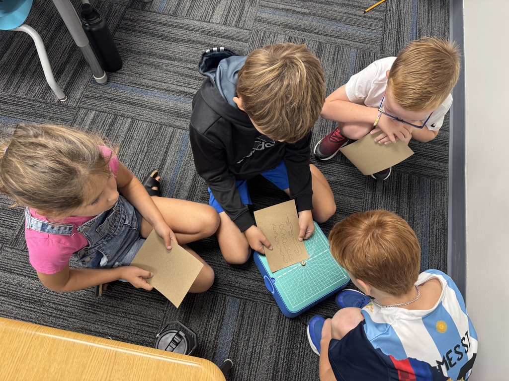 Four students sitting around the Chompsaw with one using it to cut.
