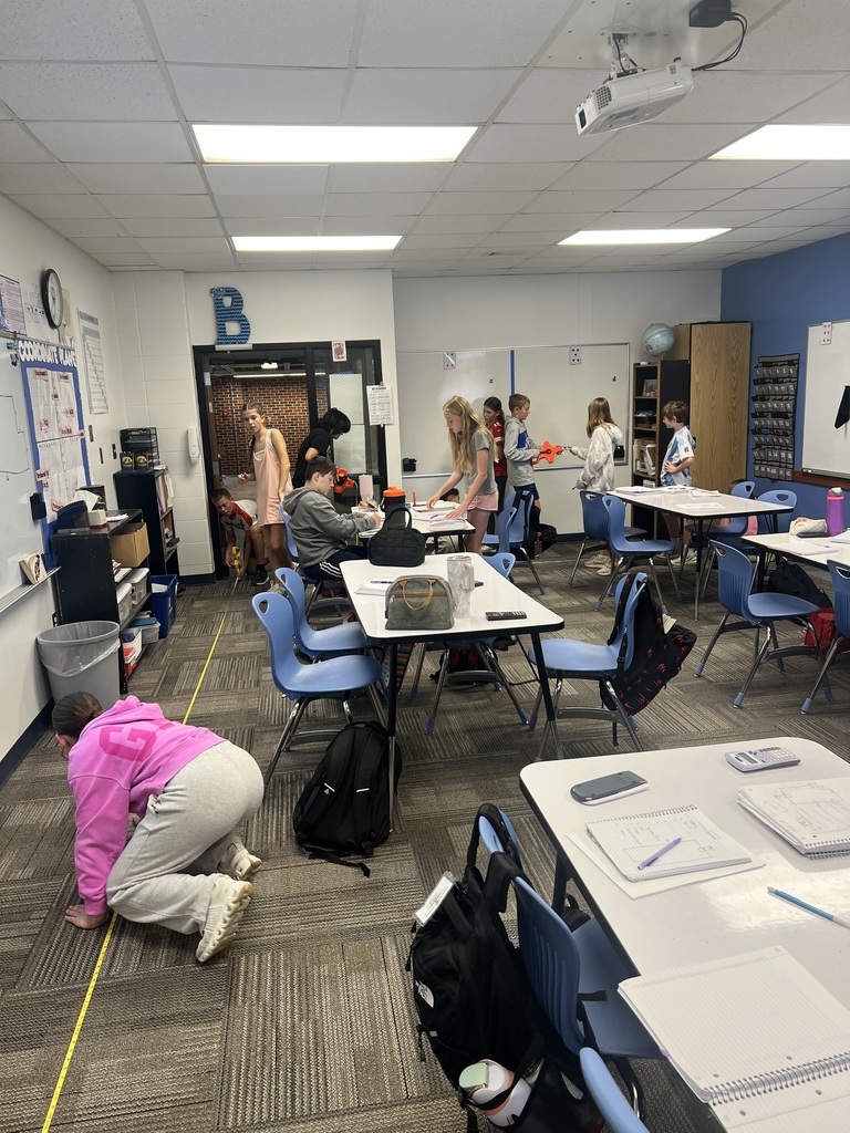 7th grade students measuring the floor and writing at a few of the tables.