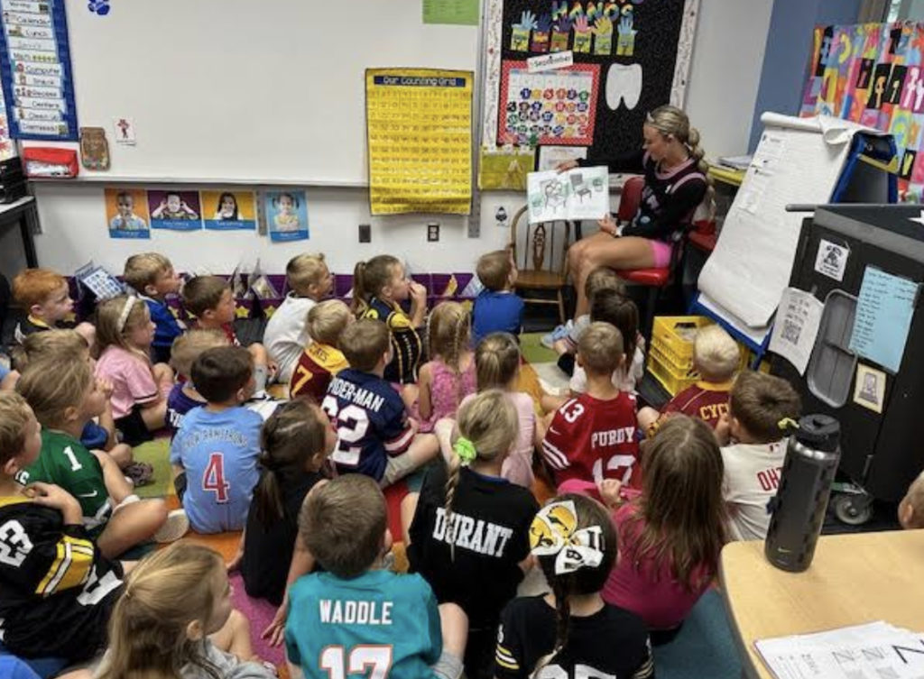 A Homecoming Court member reads to an elementary class.