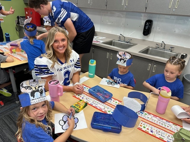 Girl wearing football jersey working with three elementary students at a table.