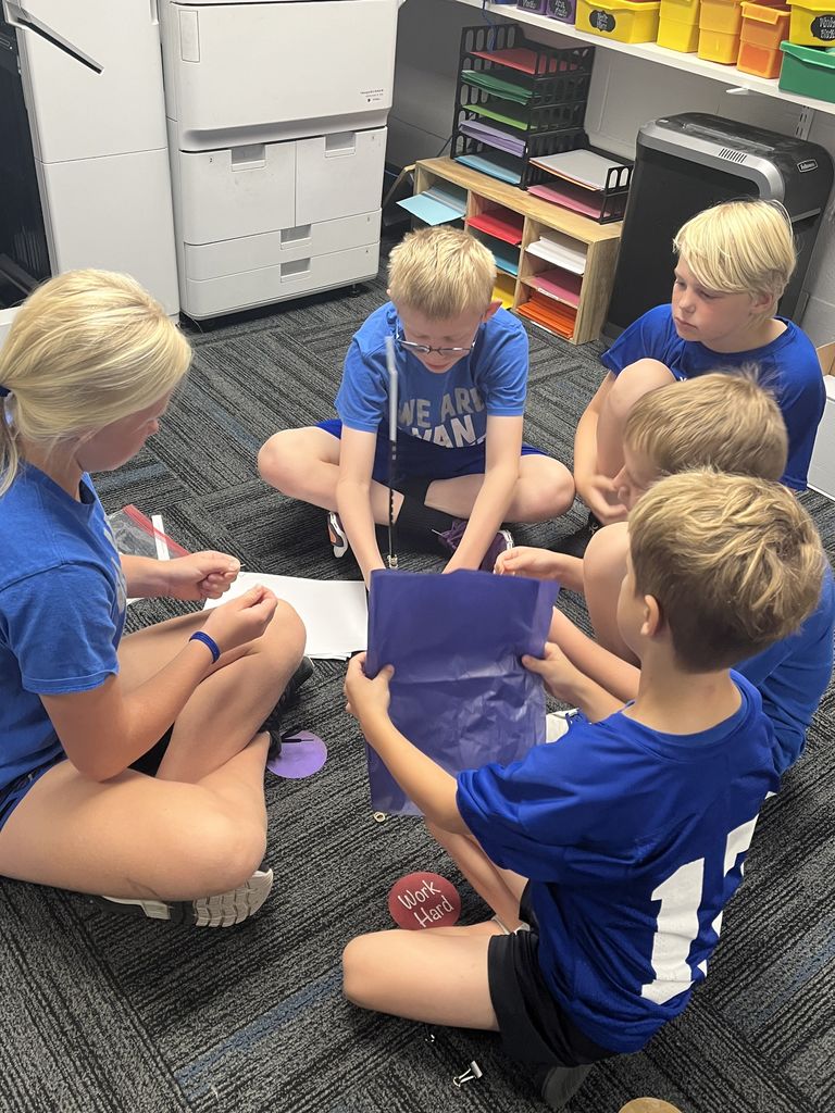 Group of five buddies sitting on the ground working together.