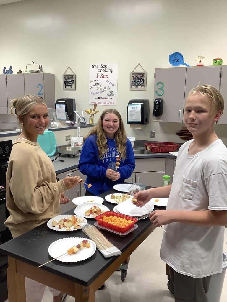 Three students smiling while making a dish with apples.