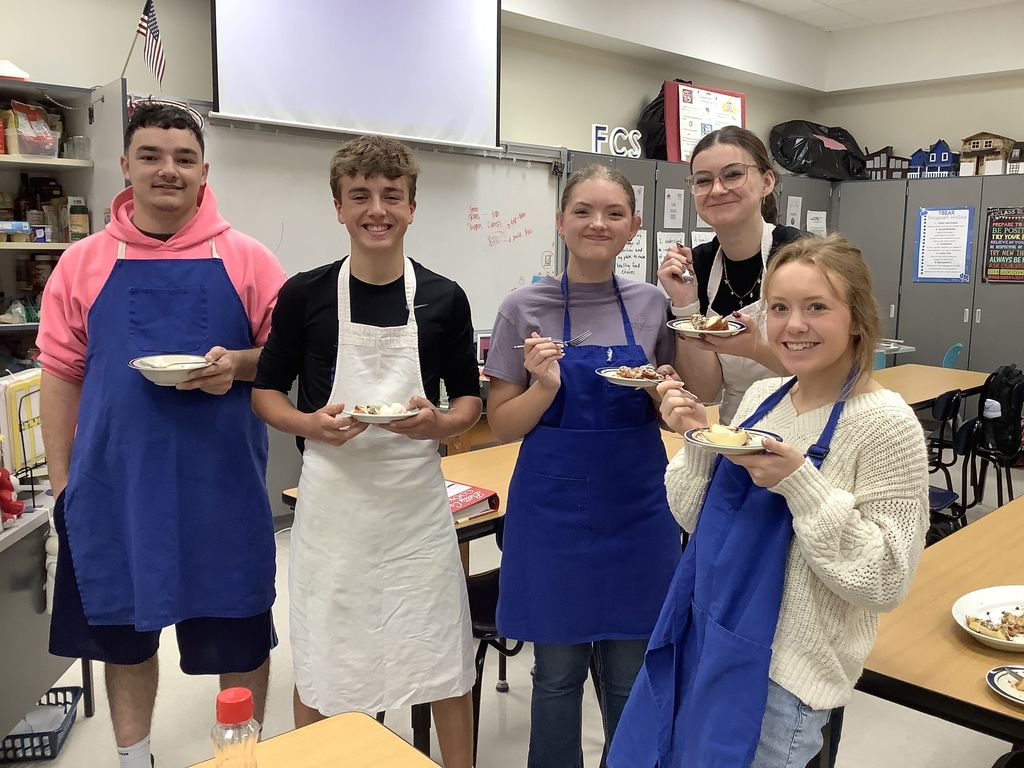 Five students smiling and tasting their prepared dishes.