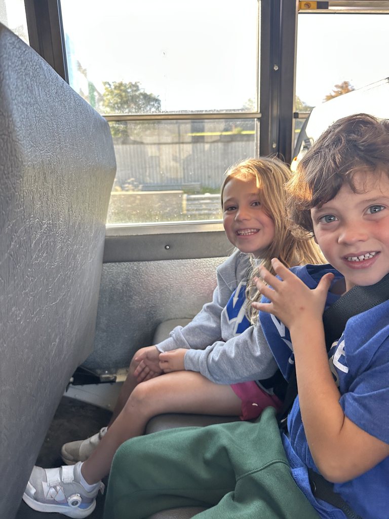 Two students smiling from their bus seat